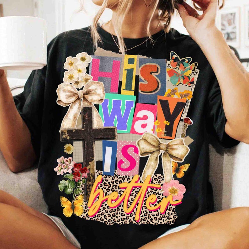 May include: Black t-shirt with a colorful graphic design. The design includes the words "His Way Is Better" in various fonts and colors, along with a cross, butterflies, flowers, and bows. The shirt has a relaxed fit.