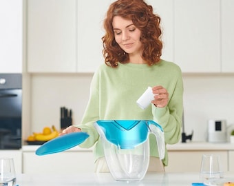 May include: A clear water filter pitcher with a turquoise lid and handle. The pitcher is partially filled with water. A white filter is being inserted into the pitcher. The pitcher is on a white countertop.