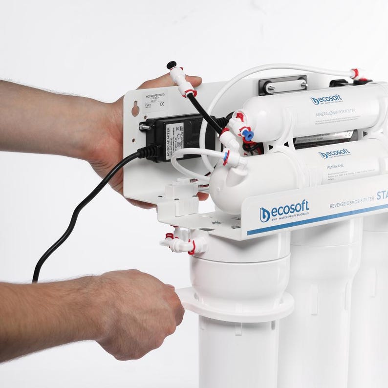 May include: A white water filtration system with multiple filters and a black power cord. The system has a white plastic housing with a blue and red logo that says "ecosoft".
