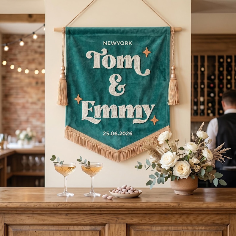 May include: A teal velvet wall banner featuring the white embroidered text NEWYORK, Tom & Emmy, and 25.06.2026. The banner is accented with three orange star icons, two side tassels, and a bottom fringe, all suspended from a wooden rod.