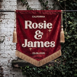 May include: A deep red velvet wall banner featuring the embroidered white text CALIFORNIA, Rosie & James, and 25.06.2026. The banner is accented with two small embroidered stars, gold-colored tassels on each side, and gold fringe at the bottom.