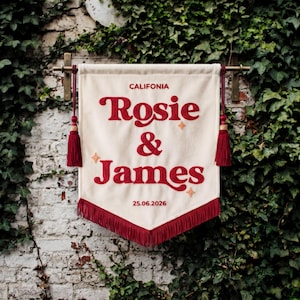 May include: A cream-colored fabric banner featuring the embroidered red text "CALIFONIA", "Rosie & James", and the date "25.06.2026". The banner includes red tassels on both sides, a red fringe at the bottom, and small embroidered star accents.