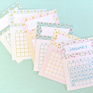 May include: A set of printable calendar cards with floral patterns. The cards are in various colors, including pink, yellow, and blue. The cards feature a blank space for writing the month and a grid for marking dates. One card has the month "January" written on it and the dates 1-31 filled in.