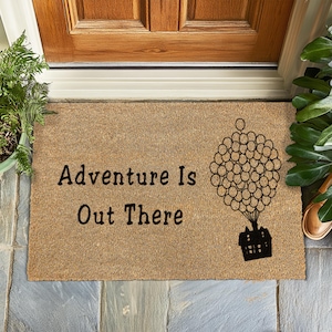 May include: A brown coir doormat with the text "Adventure is Out There" and a black silhouette of a house with balloons.