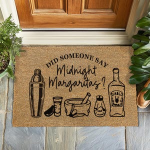 Könnte beinhalten: Eine rechteckige Fußmatte mit dem Text "DID SOMEONE SAY Midnight Margaritas?" in schwarzer Schrift. Die Matte zeigt schwarze Illustrationen eines Cocktailshakers, eines Schnapsglases, eines Mörsers und Stößels, eines Salzstreuers und einer Tequilaflasche.