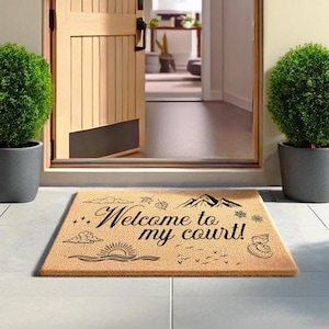 May include: A rectangular doormat made of natural fibers, featuring the text "Welcome to my court!" in elegant script. The design includes mountain, sun, cloud, and bird illustrations in black.