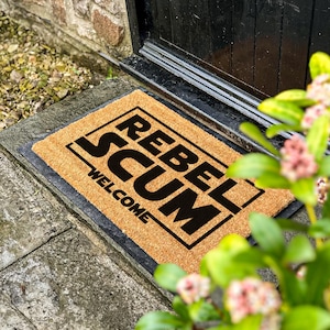May include: A brown coir doormat with black text that reads "Rebel Scum" and "Welcome".