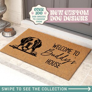 Op de afbeelding: Een rechthoekige deurmat met een hondenontwerp en de woorden "WELCOME TO Buddy's HOUSE". De mat is bruin met zwarte tekst en een zwart honden silhouet. Boven staat "OVER 100 DOG BREEDS TO CHOOSE FROM" en "NEW CUSTOM DOG DESIGNS".