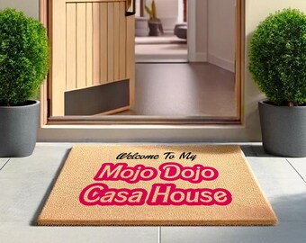 May include: A tan doormat with the text "Welcome to my Mojo Dojo Casa House" in black and pink lettering.