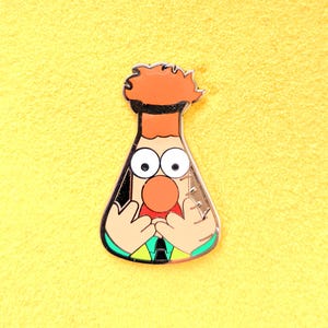 May include: A cartoon beaker with a red nose, orange hair, and wide eyes. The beaker is wearing a green and yellow shirt and a black tie. The beaker is holding its hands up to its face.