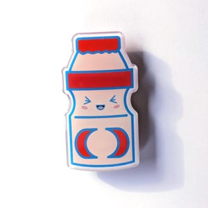 May include: A cartoon-style yogurt bottle with a red lid and blue trim. The bottle has a smiling face and two red crescent shapes on the front.