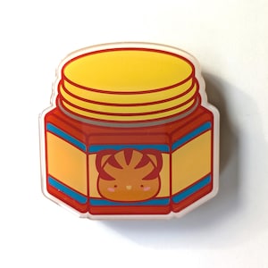 May include: A red and yellow jar with a tiger face on the front. The jar has a yellow lid with a red stripe.