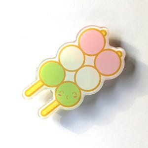 May include: A colorful, cartoon-style dango skewer with green, white, and pink dango balls. Each dango has a cute, smiling face.