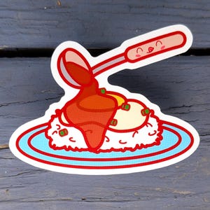 May include: A sticker featuring a cartoon illustration of a rice dish with a fried egg and sauce being poured from a spoon. The dish is on a blue plate with a red border. The spoon and the dish have smiling faces.