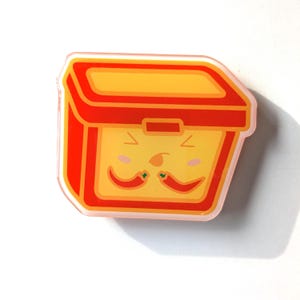 May include: A red and yellow lunchbox with a cartoon face and a mustache made of green peppers. The lunchbox has a happy expression.