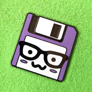 May include: Purple floppy disk enamel pin with a cartoon face wearing black-rimmed glasses. The floppy disk has a white label with a black slot.