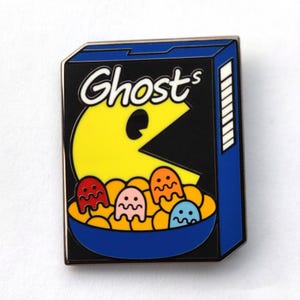 May include: A blue and black cereal box with the text "Ghost-s" on the front. A yellow Pac-Man character is eating a bowl of cereal with colorful ghosts inside.
