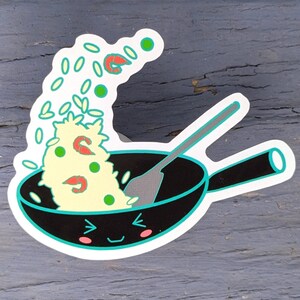 May include: A sticker featuring a cartoon illustration of fried rice in a wok. The rice is yellow with green peas and shrimp. The wok is black with a teal rim and handles, and a silver spatula. The rice has a smiling face.