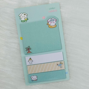 May include: A set of pastel blue sticky notes featuring cute cartoon rabbits wearing sunglasses and holding drinks. The notes have a striped pattern and a palm tree design. The text "LOVELY rabbit" is printed at the top of the notes.