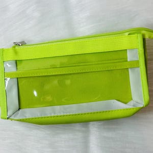 Può includere: Una pochette verde lime con cerniera e due finestre in plastica trasparente. La pochette è realizzata in tessuto resistente e ha una chiusura a zip.