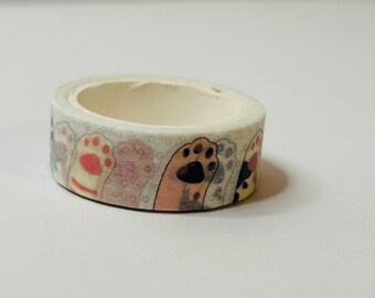 May include: A roll of white washi tape with a repeating pattern of pink, brown, and black paw prints. The paw prints are outlined in white and have a delicate lace pattern.