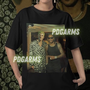May include: Black t-shirt with a graphic print of two people standing together. The text "PDGARMS" is printed on the shirt.