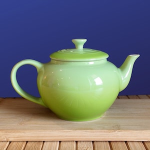 May include: A light green ceramic teapot with a glossy finish, featuring a rounded body, a curved handle, a short spout, and a matching lid with a small knob handle on top. The teapot has a smooth, uniform surface and a vibrant lime green color.