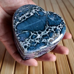 May include: A heart-shaped stone sculpture with a distinctive pattern of dark blue and white swirls. The polished surface reflects light, highlighting the intricate details of the natural stone. The sculpture is held in a hand, showcasing its size and shape.