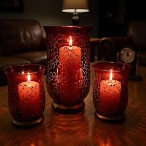 May include: Three red glass candle holders with lit candles. The holders feature a silver vine pattern. The candles are white, and the flames are bright. The holders sit on a wooden surface.