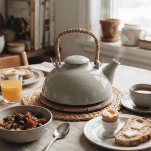 Peut inclure: Une théière en céramique gris clair avec un corps arrondi, un bec court et une anse incurvée enveloppée de rotin tressé naturel. La théière possède un couvercle assorti et repose sur un napperon tressé rond, laissant échapper de la vapeur.