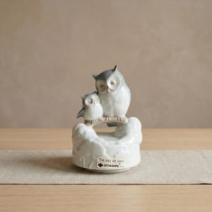 May include: A ceramic owl figurine featuring two owls perched on a branch. The owls are primarily white with gray accents. The base of the figurine is white with the text "The way we were" and the brand name "OTAGIRI".