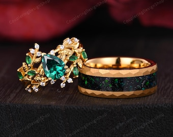 May include: A pair of gold wedding bands with green gemstones. The woman's ring features a pear-shaped emerald surrounded by smaller emeralds and diamonds set in a leafy design. The man's ring has a black and green inlay.