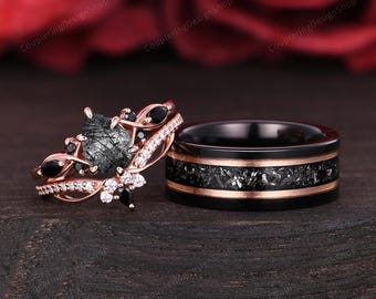 Puede incluir: Un juego de dos anillos. Uno es de oro rosa con una piedra negra, detalles negros y pequeñas piedras blancas. El otro es negro con una banda moteada negra y plateada y detalles en oro rosa. Los anillos están sobre una superficie de madera oscura.