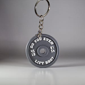May include: Grey metal keychain shaped like a weight plate with the text "Do you even lift bro?" and the weight "45 lb 81 sh" printed on it.