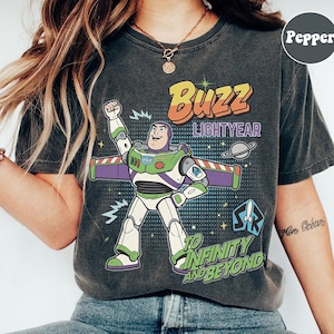 May include: Dark grey t-shirt with a Buzz Lightyear graphic. The design includes the text "Buzz Lightyear" and "To Infinity and Beyond" with a cartoon image of the character. The shirt has a vintage, worn appearance.