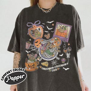 Puede incluir: Camiseta gris oscuro con un diseño temático de Halloween. El diseño incluye personajes de dibujos animados, calabazas, murciélagos y el texto "BOO". La camiseta tiene un aspecto vintage y desgastado.