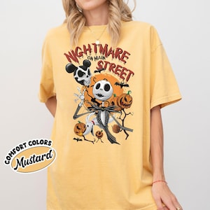 May include: Mustard-colored t-shirt featuring a graphic of Jack Skellington from The Nightmare Before Christmas, with the text "Nightmare on Main Street." The design includes pumpkins, bats, and a Mickey Mouse-inspired skull.
