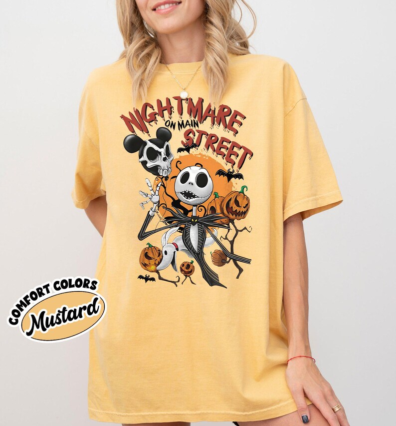 May include: Mustard-colored t-shirt featuring a graphic of Jack Skellington from The Nightmare Before Christmas, with the text "Nightmare on Main Street." The design includes pumpkins, bats, and a Mickey Mouse-inspired skull.
