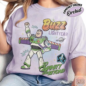 May include: Orchid-coloured t-shirt with a graphic of Buzz Lightyear from Toy Story. The design includes the words "Buzz Lightyear" and "To Infinity and Beyond" with a cartoon image of Buzz Lightyear in his space suit.