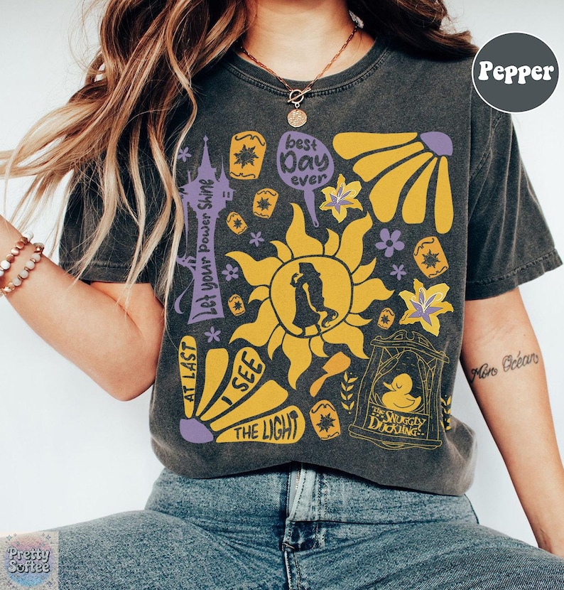 K&ouml;nnte beinhalten: Dunkelgraues T-Shirt mit einem farbenfrohen Grafikdesign mit einer Sonne, Blumen und Text, der "Best Day Ever", "I See The Light" und "Let Your Power Shine" lautet. Das Shirt hat auch eine Silhouette eines Paares.