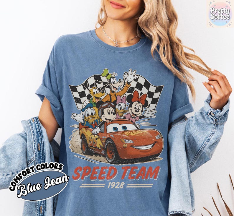 K&ouml;nnte beinhalten: Blaues Jeans-T-Shirt mit einer Grafik von Disney-Figuren in einem Rennwagen. Das Design umfasst Micky Maus, Donald Duck, Goofy sowie Minnie und Daisy Duck. Der Text "SPEED TEAM 1928" ist rot gedruckt.