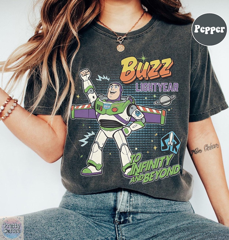 May include: Dark grey t-shirt with a Buzz Lightyear graphic. The design includes the text "Buzz Lightyear" and "To Infinity and Beyond" with a cartoon image of the character. The shirt has a vintage, worn appearance.