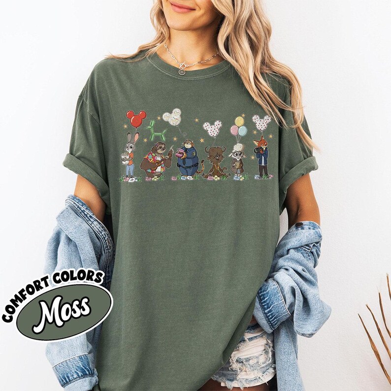 Puede incluir: Camiseta Comfort Colors verde musgo con un dise&ntilde;o de dibujos animados de personajes de animales sosteniendo globos. El dise&ntilde;o incluye un conejo, un perezoso, un oso y un zorro. La camiseta tiene mangas enrolladas y un ajuste relajado.