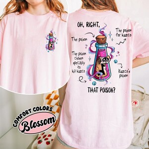 May include: A light pink t-shirt with a graphic of a potion bottle containing a cartoon character. The back of the shirt features the text "OH, RIGHT, THAT POISON?" with additional text and arrows pointing to the bottle and its contents.