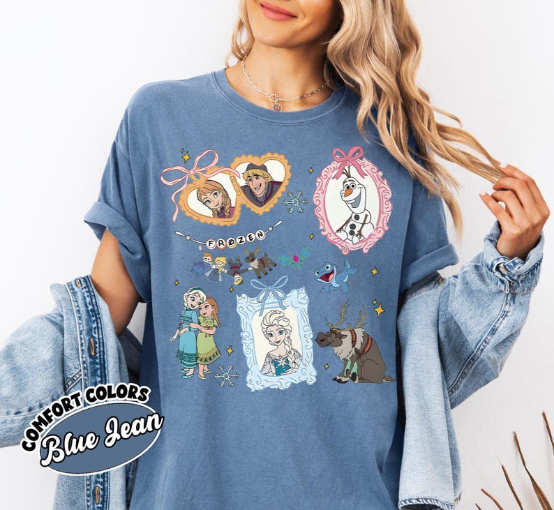 May include: Blue jean-colored t-shirt featuring illustrations of characters from the movie "Frozen." The design includes framed portraits of Anna, Elsa, Kristoff, and Olaf, along with other characters and the word "Frozen."