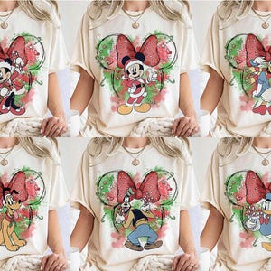 May include: Cream-colored t-shirts featuring various Disney characters in Christmas attire. Each shirt showcases a character like Mickey Mouse, Minnie Mouse, Donald Duck, or Goofy, set against a festive bow and holiday-themed background. The designs incorporate red, green, and white colors.