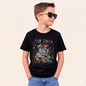 May include: Black t-shirt featuring a colorful graphic of Toy Story characters with the words "TOY STORY" in rainbow colors. The design includes Woody, Buzz Lightyear, and other characters from the movie. The shirt is worn by a person wearing sunglasses.