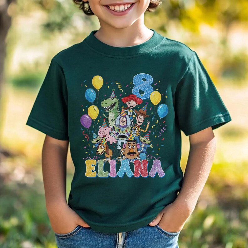 May include: Dark green t-shirt featuring a colorful graphic of Toy Story characters, balloons, confetti, and the number 8. The name "ELIANA" is written in colorful letters below the characters. A fun and festive design.