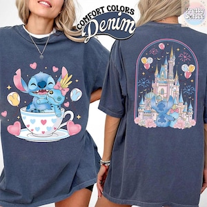May include: Denim blue t-shirt featuring a cartoon character in a teacup with hearts and the text "Comfort Colors Denim". The back of the shirt shows a castle scene with the same character. The shirt has short sleeves.