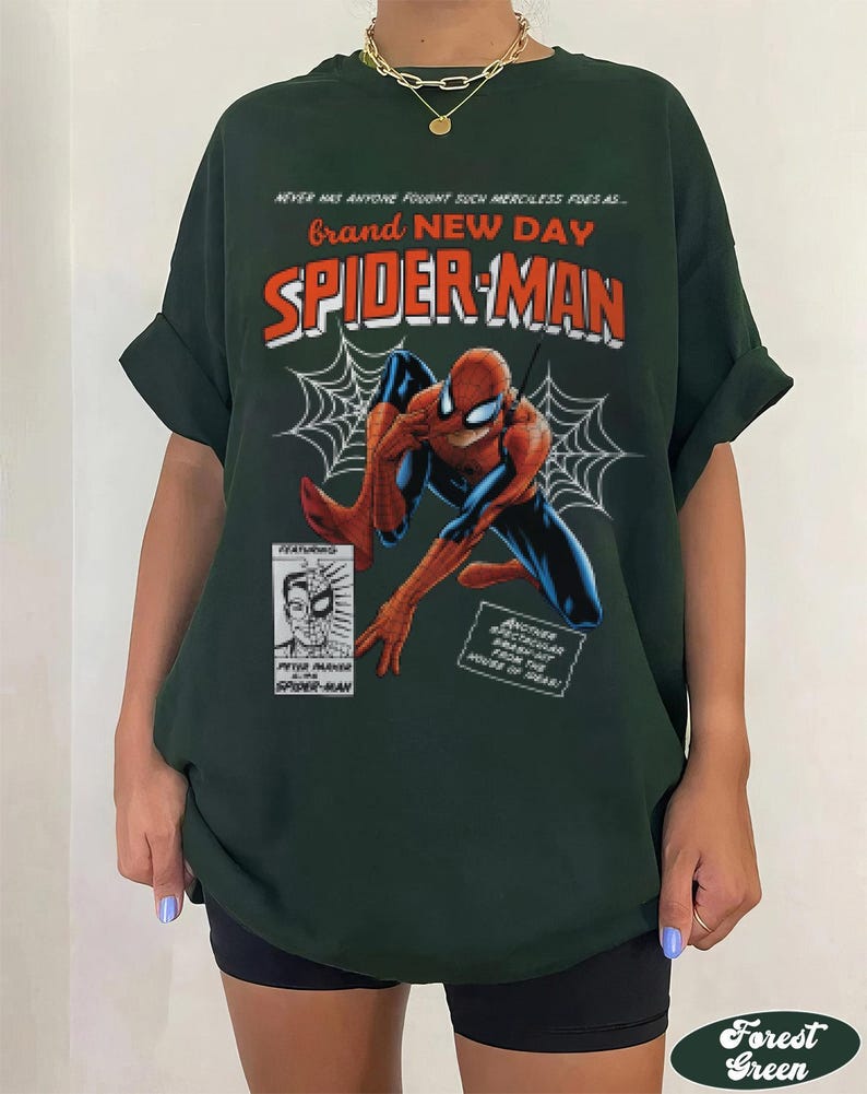 K&ouml;nnte beinhalten: Forstgr&uuml;nes T-Shirt mit einem Spider-Man-Motiv. Das Design enth&auml;lt die W&ouml;rter "Brand New Day" und "Spider-Man" in Rot und Orange, mit einer Comic-Illustration von Spider-Man und einem Spinnennetz.